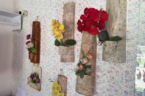 Arranjos florais artesanais expostos em suportes de madeira